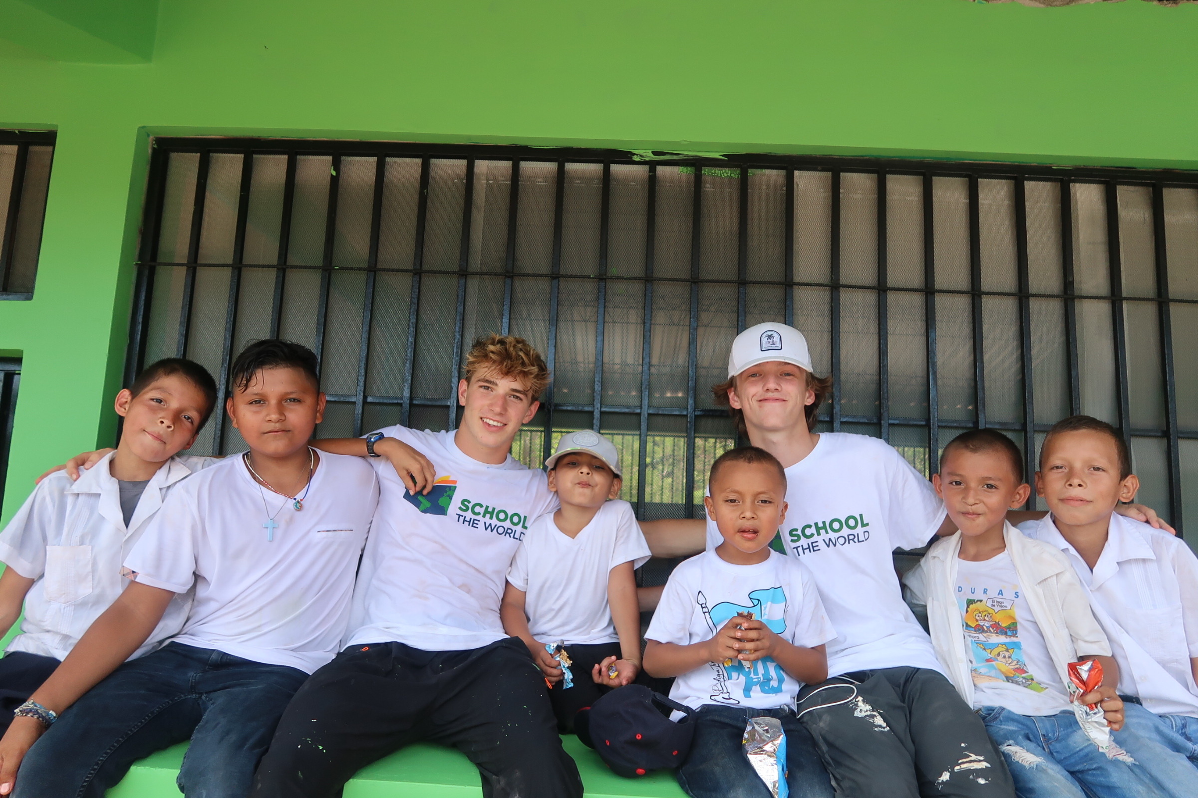 Two students hugging children at a school in Honduras during a Service Learning Trip, fostering connections and making a meaningful impact.